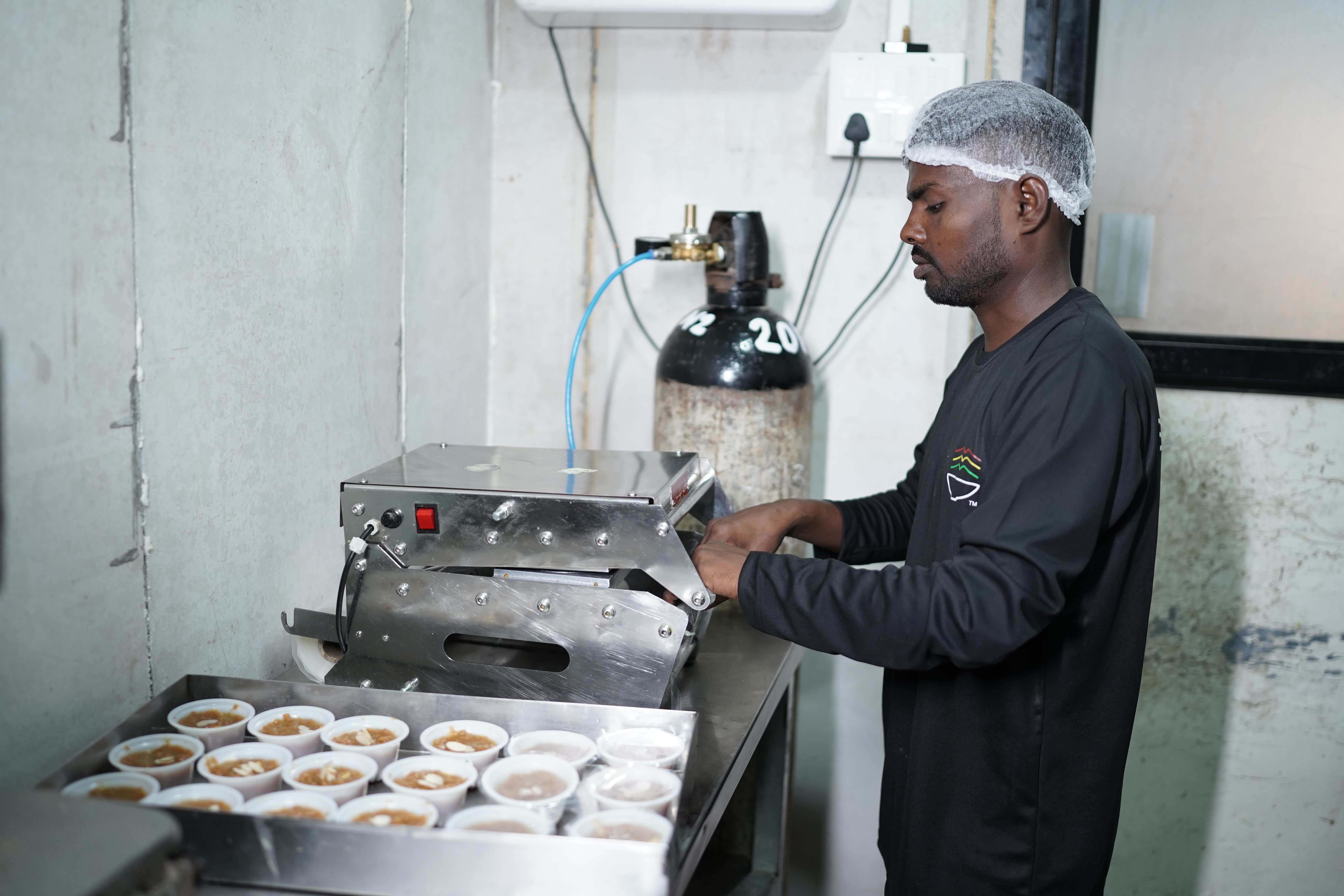 Team member operating semi-automated sealing equipment for individual mithai portions